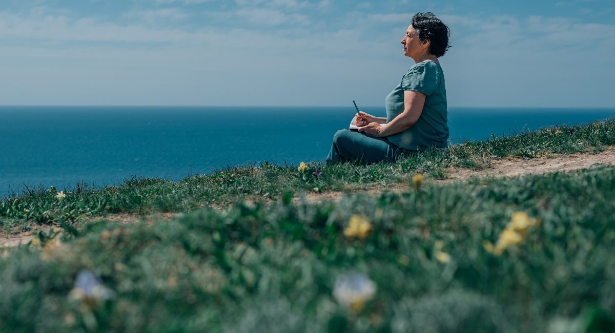 adult woman writes plans in a diary in the summer on a mountain against the background of sky, sea