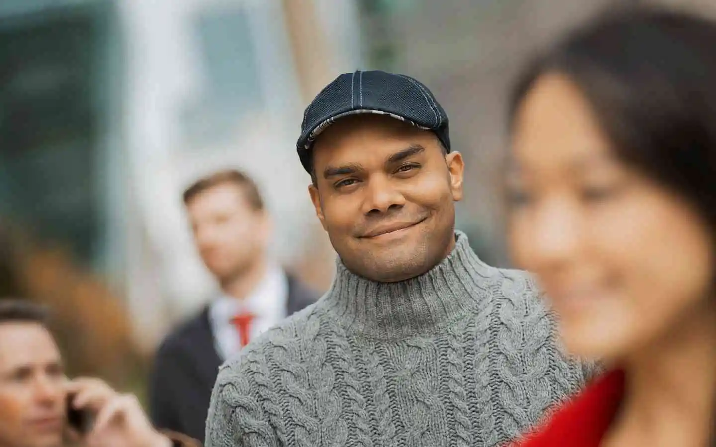A smiling man in a cap and sweater standing next to a woman.