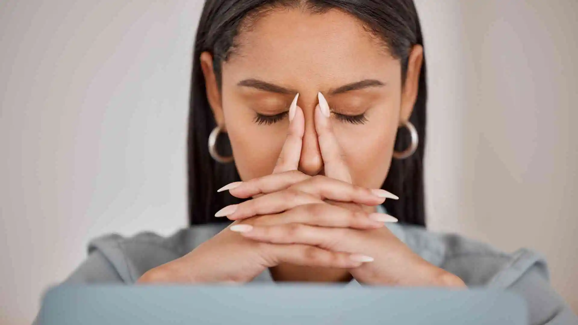 A woman with a laptop, her hands covering her face in surprise or shock.