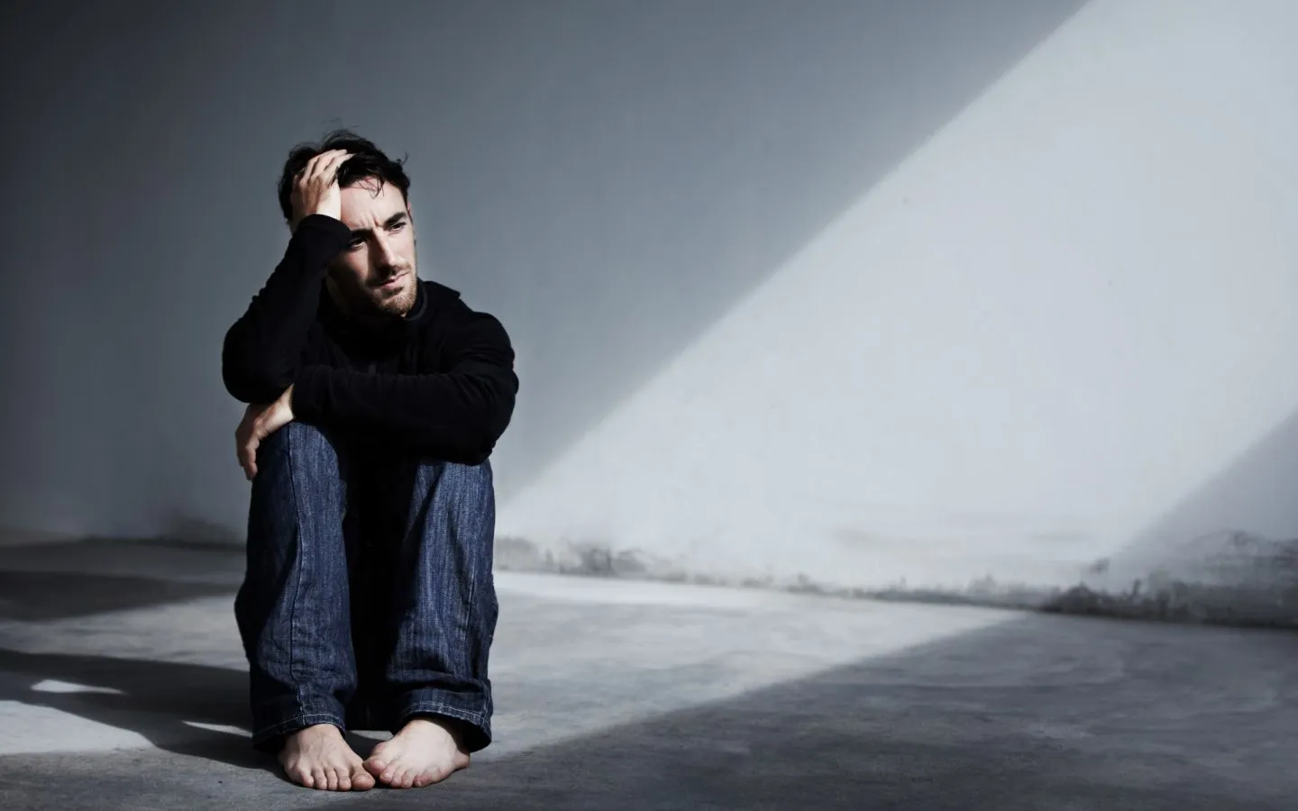 A man sitting on the floor, looking distressed, with his hands placed on his head in frustration.