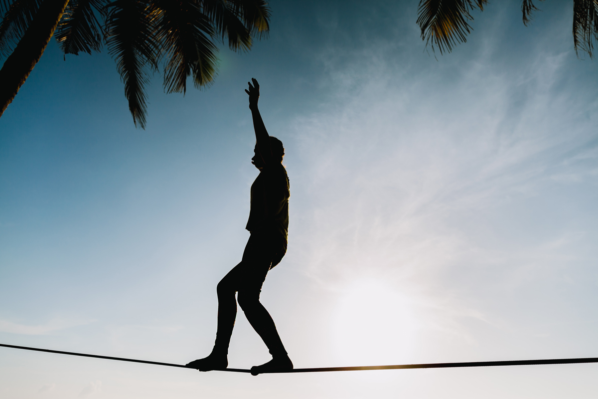 A silhouette of a man balancing on a tightrope against a sunset backdrop.
