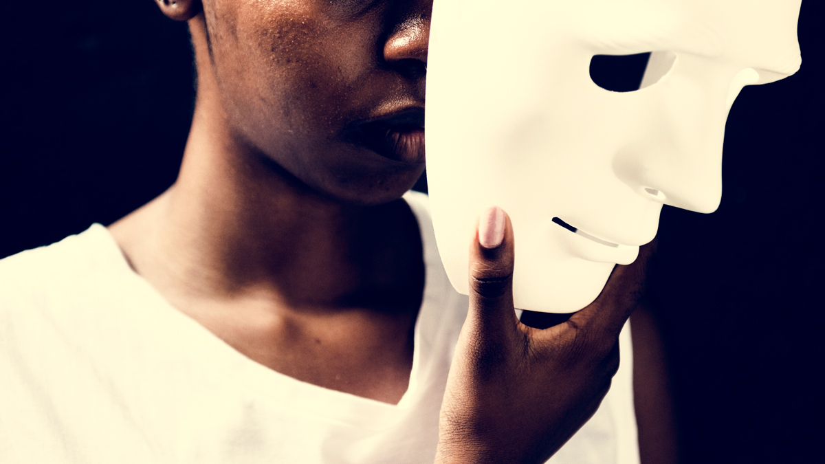 A woman holds a white mask in front of her face, partially obscuring her features and creating a mysterious atmosphere.