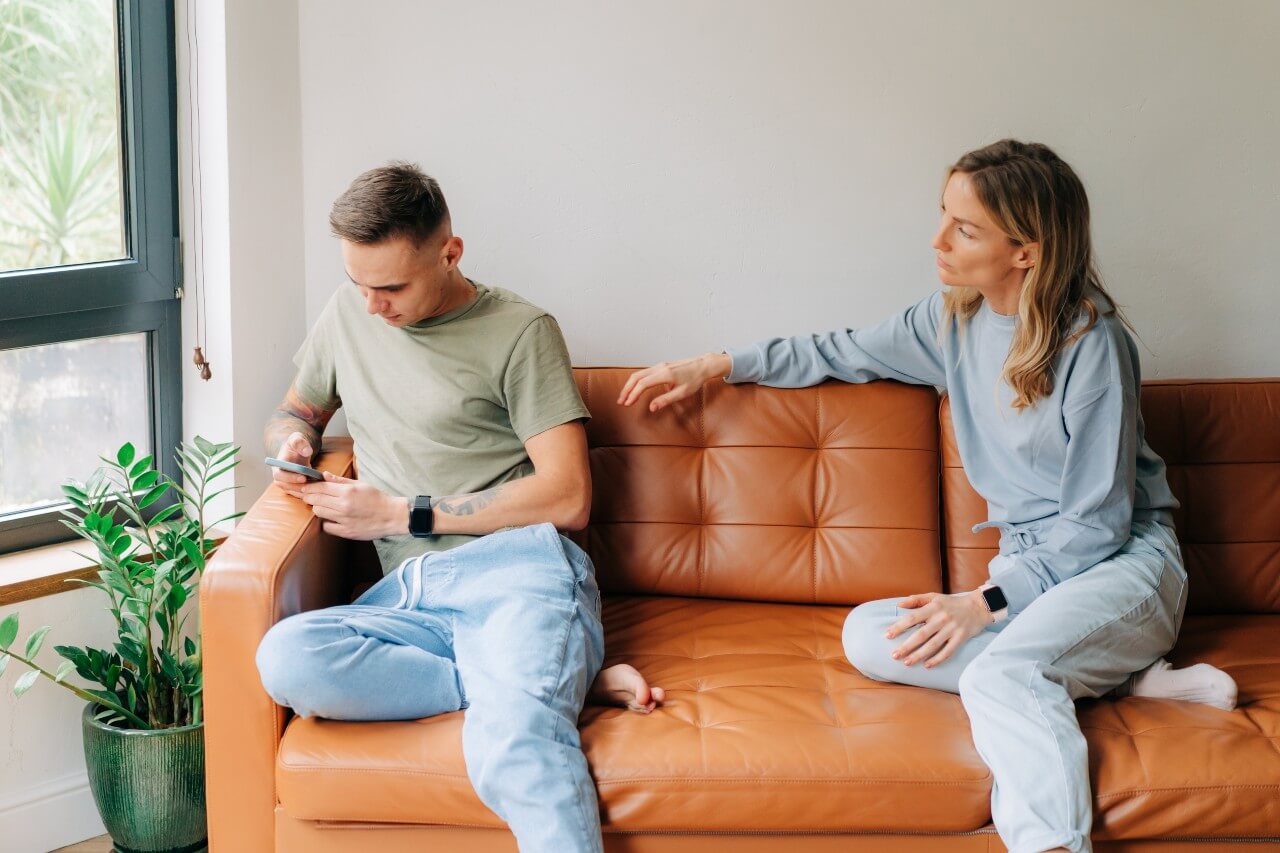 A man and woman sit on a couch, both focused on their phones, with a relaxed atmosphere in the living room.