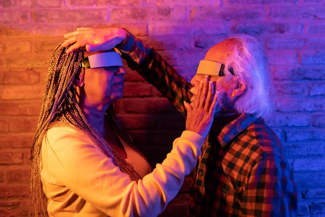 Elderly couple exploring virtual reality, hands touching, surrounded by colorful lighting