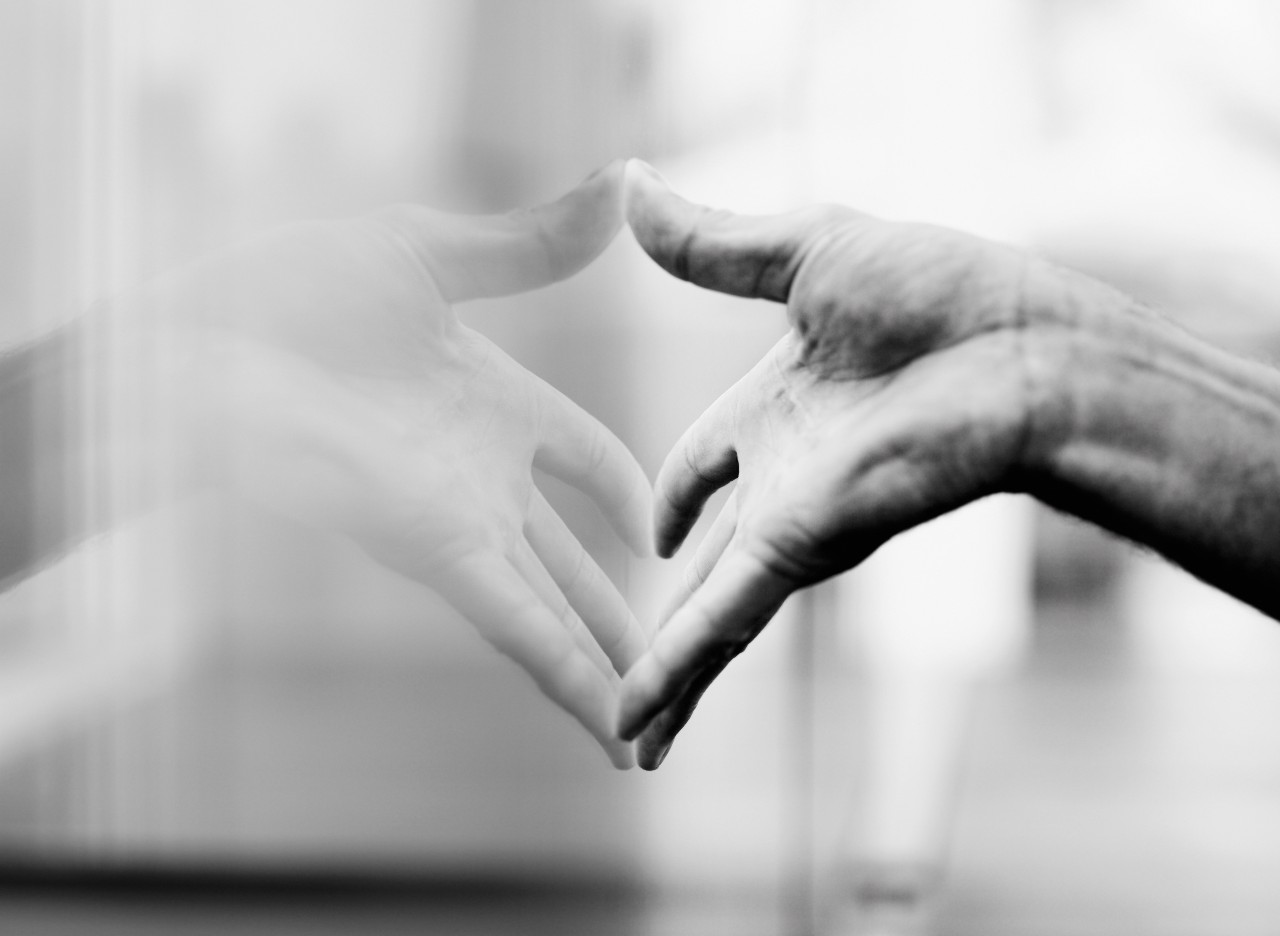 Hand reaching toward its reflection on glass, symbolizing self-awareness and introspection in people-pleasing patterns.