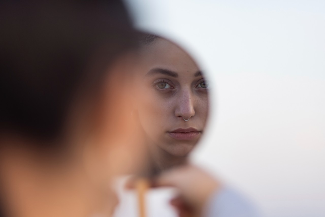 A woman with her eyes closed gazes into a mirror, reflecting a moment of introspection and self-reflection.