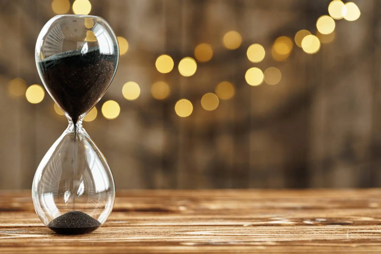 Hourglass on wooden desk against blurred lights