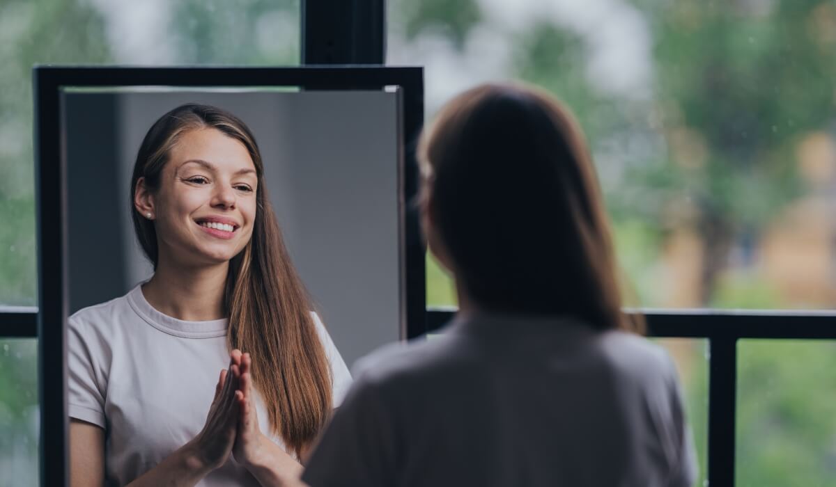 A woman smiles gently at herself in the mirror, reflecting calm and gratitude. Image used by Get Reconnected Psychotherapy and Counselling Services. Contact info@getreconnected.ca.