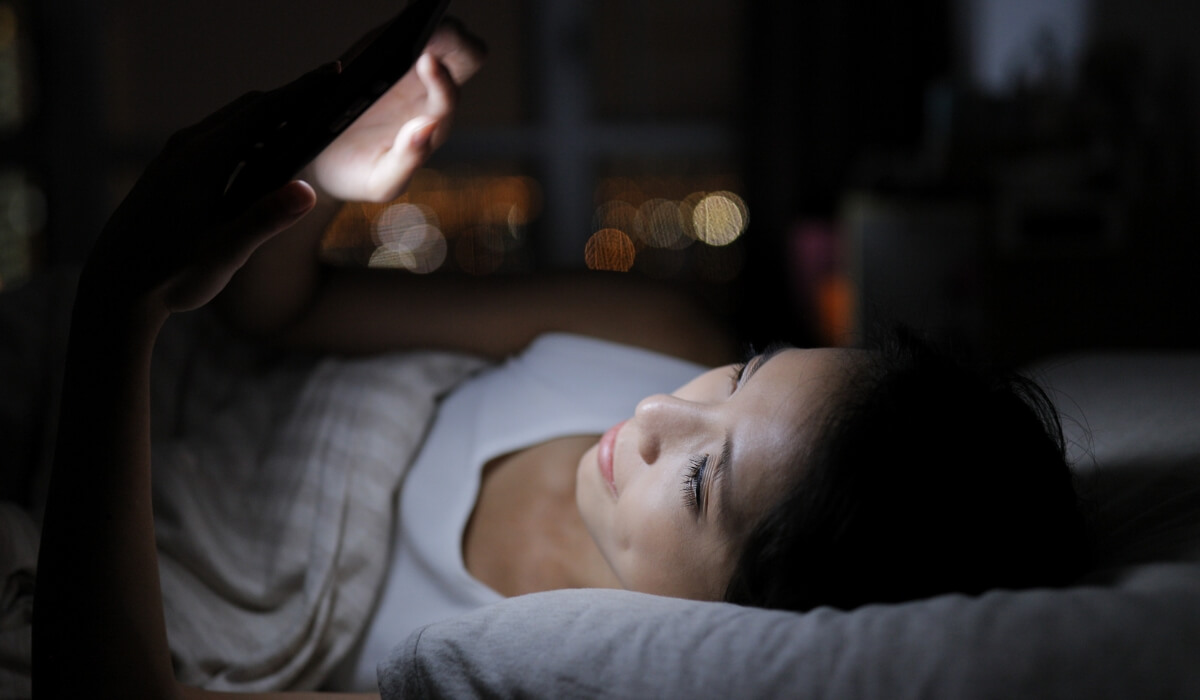 A woman lies in bed at night looking at her phone, highlighting digital habits linked to modern stress. Image used by Get Reconnected Psychotherapy and Counselling Services. Contact info@getreconnected.ca.