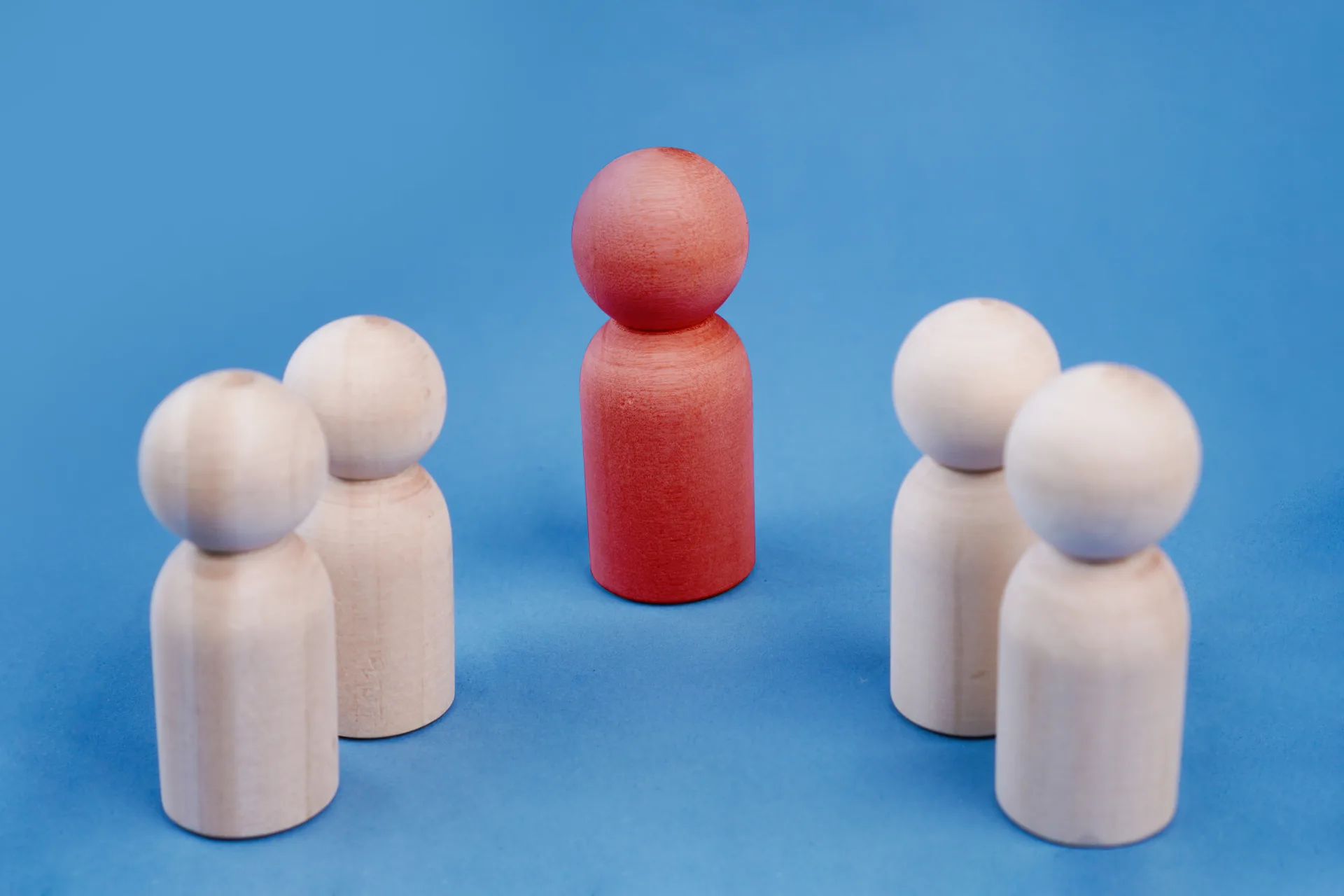 Red wooden figure standing apart from groups of natural wooden figures
