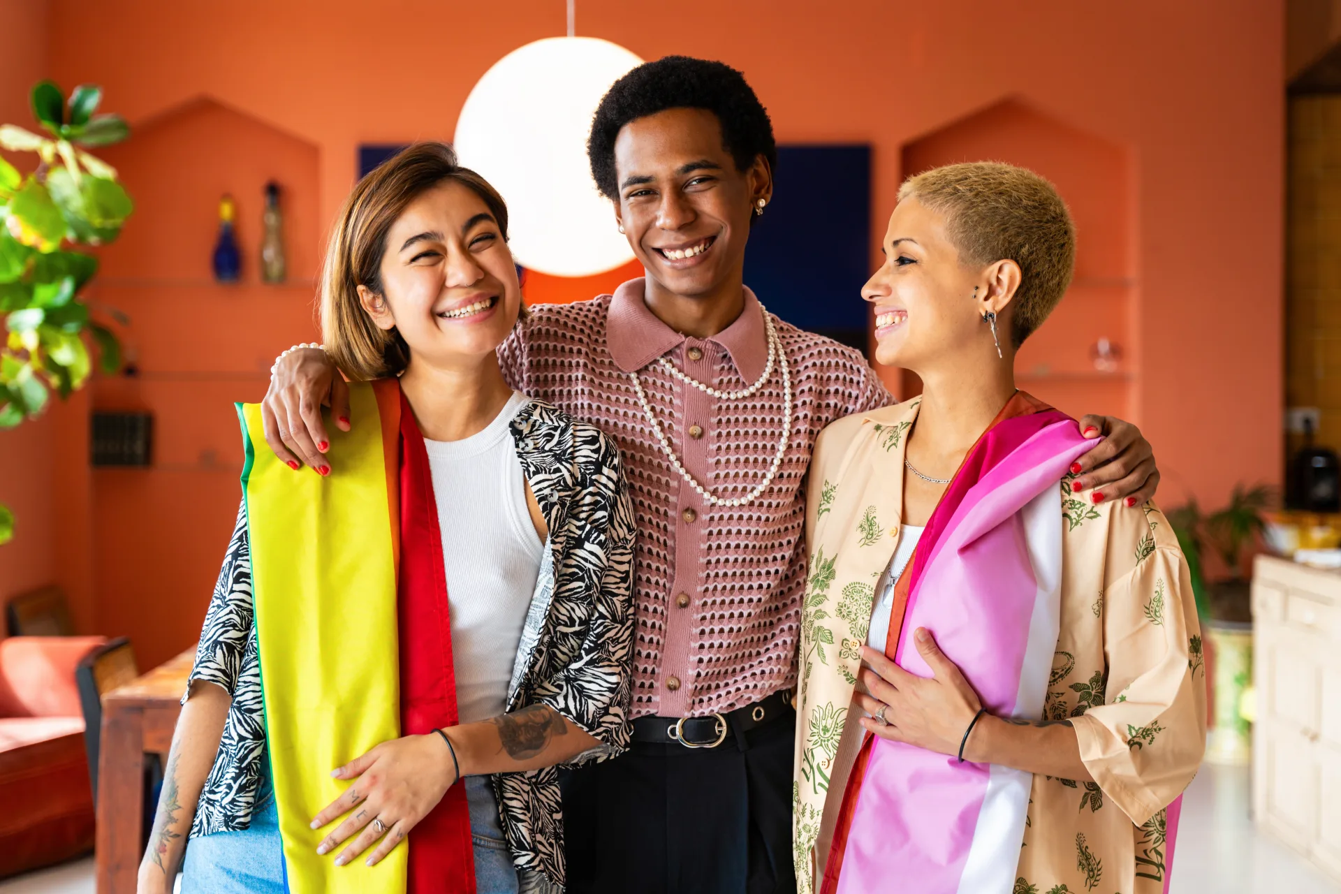 Three friends smiling indoors with Pride flags