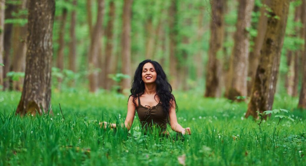 Positive brunette in casual clothes meditating in the forest at daytime