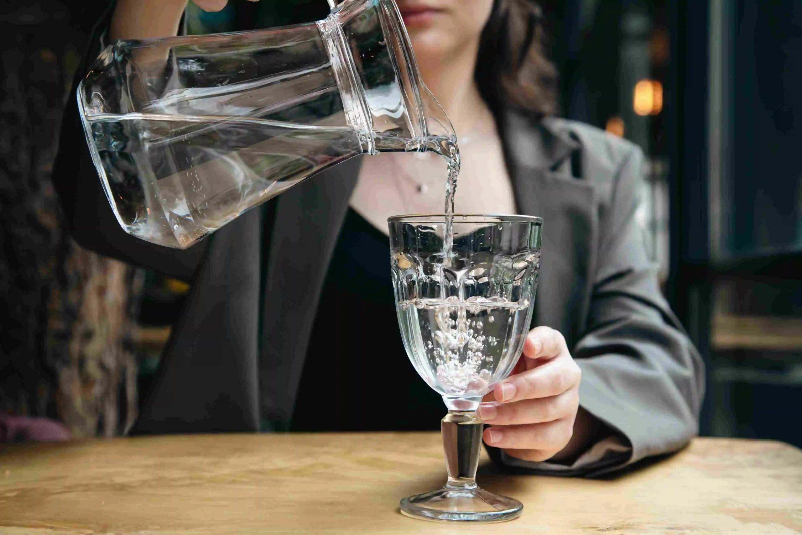 Pouring water from a jug into a glass held by a woman.