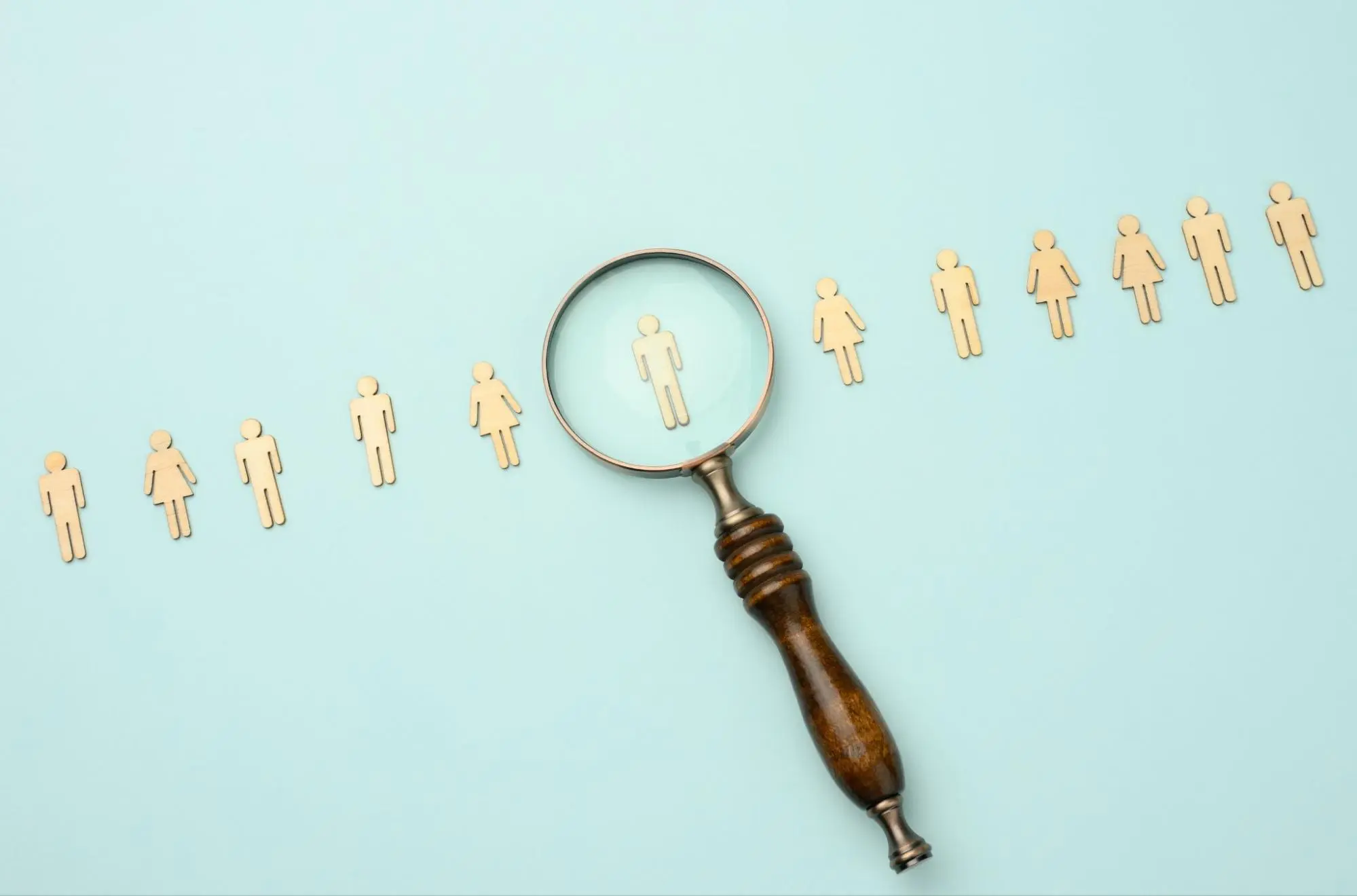 A magnifying glass examines a group of people with a wooden stick.