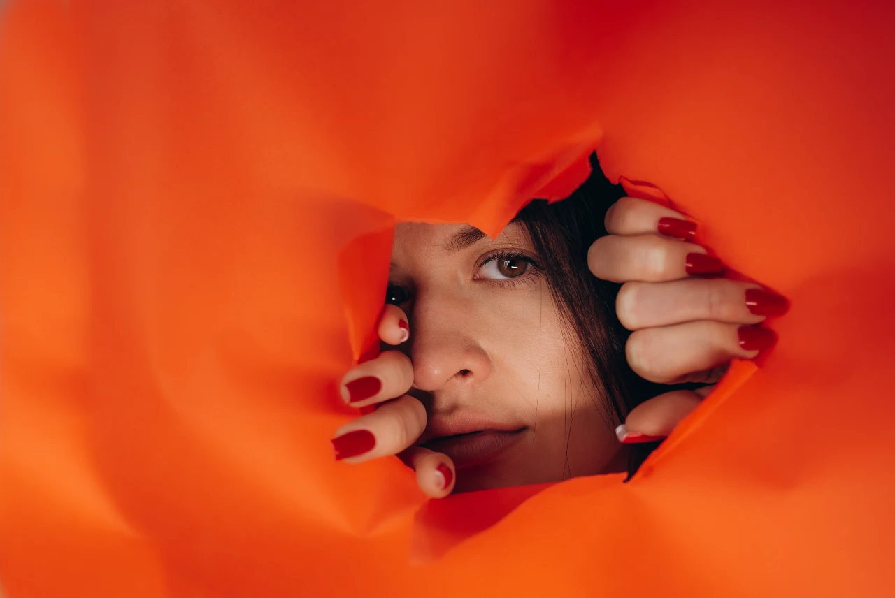 a woman looking through a hole in orange paper wall