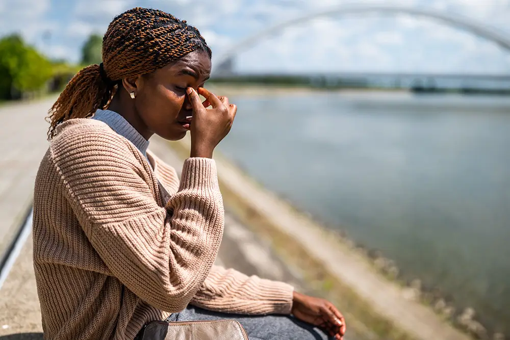 Young beautiful woman is sitting by the river in the city. She is having headache.