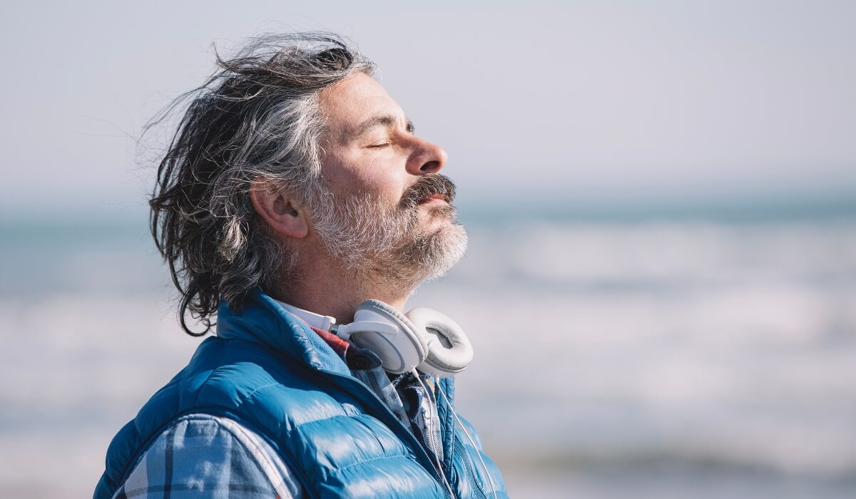 A man stands alone on a quiet beach with eyes closed, finding emotional calm. Image used by Get Reconnected Psychotherapy and Counselling Services. Contact info@getreconnected.ca.